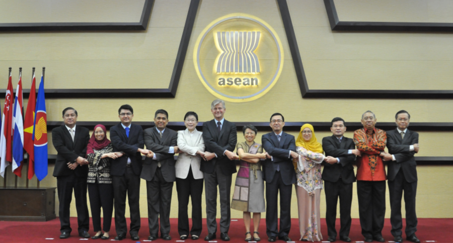 Group portrait of officials holding hands in front of ASEAN logo and flags.